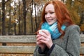 Redhead girl with cup in autumn park, yellow leaves and trees Royalty Free Stock Photo
