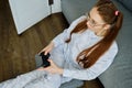 Redhead girl with glasses, with long tails sits on the floor in a half-turn leaning on a sofa with a game console, shot Royalty Free Stock Photo