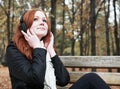 Redhead girl with headphones listen music on player in city park, fall season Royalty Free Stock Photo