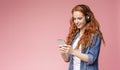 Redhead girl listening music on her smartphone with modern headphones Royalty Free Stock Photo