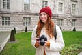 Redhead girl photographer takes photos on professional camera outdoors, captures streetstyle shots, looks excited while Royalty Free Stock Photo