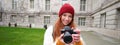 Redhead girl photographer takes photos on professional camera outdoors, captures streetstyle shots, looks excited while Royalty Free Stock Photo