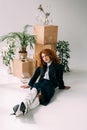 Redhead girl posing near wooden boxes, glasses and plants on grey with sunlight Royalty Free Stock Photo