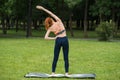 Redhead girl standing on a mat on the grass in the park stretching her arms. Royalty Free Stock Photo