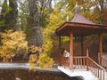 Redhead girl stands in a gazebo over muddy water in an autumn park