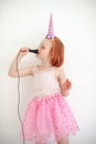 A girl in a unicorn costume sings into a microphone