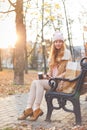 Redhead girl in warm clothes sitting with coffee on wooden bench in autumn park. Royalty Free Stock Photo
