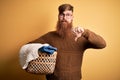 Redhead Irish man with beard doing housework laundry over yellow background with angry face, negative sign showing dislike with