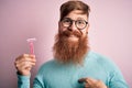 Redhead Irish man with beard holding beauty razor for shaving and skin care over pink background with surprise face pointing Royalty Free Stock Photo