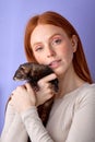 redhead lady posing with ferret isolated in studio on purple background, cute domestic animal Royalty Free Stock Photo