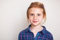 Redhead little girl in blue plaid shirt against wall. Royalty Free Stock Photo