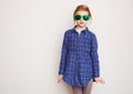 Redhead little girl in green sunglasses posing against wall. Royalty Free Stock Photo