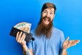 Redhead man with long beard holding wallet euro banknotes celebrating achievement with happy smile and winner expression with Royalty Free Stock Photo