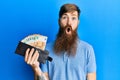 Redhead man with long beard holding wallet euro banknotes scared and amazed with open mouth for surprise, disbelief face Royalty Free Stock Photo