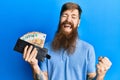 Redhead man with long beard holding wallet euro banknotes screaming proud, celebrating victory and success very excited with Royalty Free Stock Photo