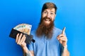 Redhead man with long beard holding wallet euro banknotes smiling happy pointing with hand and finger to the side Royalty Free Stock Photo