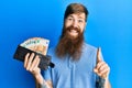 Redhead man with long beard holding wallet euro banknotes smiling with an idea or question pointing finger with happy face, number Royalty Free Stock Photo