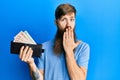 Redhead man with long beard holding wallet united kingdom pounds covering mouth with hand, shocked and afraid for mistake
