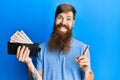 Redhead man with long beard holding wallet united kingdom pounds smiling happy pointing with hand and finger to the side
