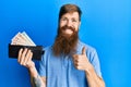 Redhead man with long beard holding wallet united kingdom pounds smiling happy and positive, thumb up doing excellent and approval