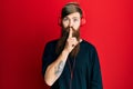 Redhead man with long beard listening to music using headphones asking to be quiet with finger on lips Royalty Free Stock Photo