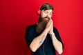 Redhead man with long beard listening to music using headphones sleeping tired dreaming and posing with hands together while Royalty Free Stock Photo