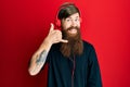 Redhead man with long beard listening to music using headphones smiling doing phone gesture with hand and fingers like talking on Royalty Free Stock Photo