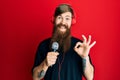 Redhead man with long beard singing song using microphone and wearing headphones doing ok sign with fingers, smiling friendly Royalty Free Stock Photo