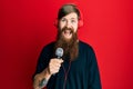 Redhead man with long beard singing song using microphone and wearing headphones looking positive and happy standing and smiling Royalty Free Stock Photo