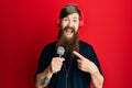 Redhead man with long beard singing song using microphone and wearing headphones smiling happy pointing with hand and finger Royalty Free Stock Photo