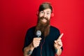 Redhead man with long beard singing song using microphone and wearing headphones smiling happy pointing with hand and finger to Royalty Free Stock Photo