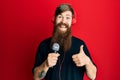 Redhead man with long beard singing song using microphone and wearing headphones smiling happy and positive, thumb up doing Royalty Free Stock Photo