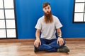 Redhead man with long beard sitting on the floor at empty room making fish face with lips, crazy and comical gesture