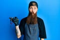 Redhead man with long beard tattoo artist wearing professional uniform and gloves making fish face with lips, crazy and comical Royalty Free Stock Photo