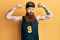 Redhead man with long beard wearing basketball uniform showing muscles skeptic and nervous, frowning upset because of problem