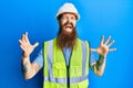 Redhead man with long beard wearing safety helmet and reflective jacket crazy and mad shouting and yelling with aggressive Royalty Free Stock Photo