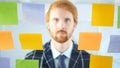 Redhead Man Looking Through Sticky Notes Attached on Glass in Office Royalty Free Stock Photo