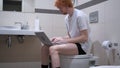 Redhead Man Typing on Laptop, Sitting on Toilet Commode