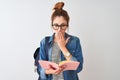 Redhead student woman wearing backpack reading book over isolated white background cover mouth with hand shocked with shame for Royalty Free Stock Photo