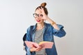 Redhead student woman wearing backpack reading book over isolated white background with happy face smiling doing ok sign with hand Royalty Free Stock Photo