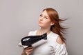 Redhead woman with blow drying hair holding hair dryer on gray wall studio background Royalty Free Stock Photo