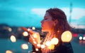 Redhead woman sending kiss with fairy light garland at evening