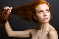 Redhead woman holding her healthy and shiny hair, studio grey Royalty Free Stock Photo