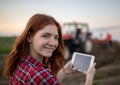 Redhead woman using tablet in agriculture standinf in field in front of tractor