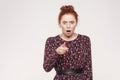 Redhead woman wearing flowers dress, opening mouths widely, having surprised shocked looks, pointing finger at camera.