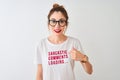 Redhead woman wearing funny t-shirt with irony comments over isolated white background with surprise face pointing finger to