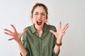 Redhead woman wearing green shirt and glasses standing over isolated white background crazy and mad shouting and yelling with Royalty Free Stock Photo