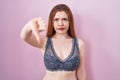 Redhead woman wearing lingerie over pink background looking unhappy and angry showing rejection and negative with thumbs down Royalty Free Stock Photo