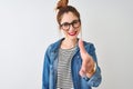 Redhead woman wearing striped t-shirt denim shirt and glasses over isolated white background smiling friendly offering handshake Royalty Free Stock Photo