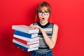 Redhead young woman holding a pile of books afraid and shocked with surprise and amazed expression, fear and excited face Royalty Free Stock Photo